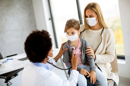 Mother with his little daughter at the pediatrician examination by African american female doctorの写真素材