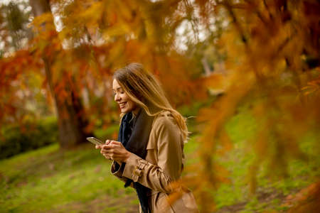 Pretty young woman using mobile phone in the autumn parkの写真素材