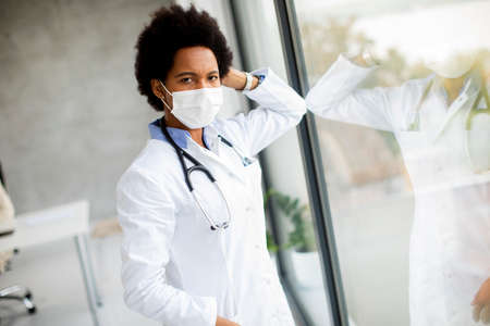 Black female doctor standing by the medical office window with facial protective maskの写真素材