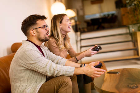Handsome young couple playing video games at home, sitting on sofa and enjoying themselves