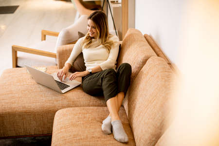 Young beautiful woman using a laptop on the sofa at homeの写真素材