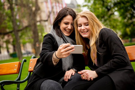 Young female tourists taking selfie with mobile photo on the bench in centre of Vienna, Austriaの写真素材