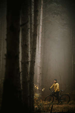 Handsome young man taking a brake during biking through autumn forestの写真素材