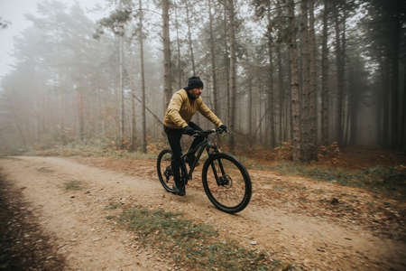 Handsome young man biking through autumn forestの写真素材