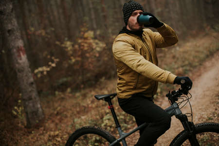 Handsome young man taking a brake during biking through autumn forestの写真素材
