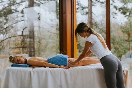 Beautiful young woman lying and having leg massage in spa salon during winter seasonの写真素材