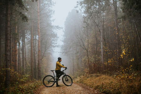 Handsome young man taking a brake during biking through autumn forestの写真素材