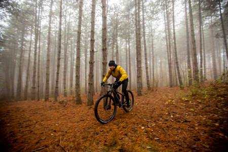 Handsome young man biking through autumn forest