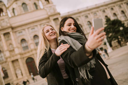 Young female tourists taking selfie with mobile photo on the street in centre of Vienna, Austria