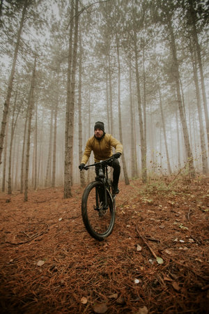 Handsome young man biking through autumn forestの写真素材