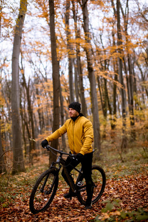 Handsome young man taking a brake during biking through autumn forestの写真素材