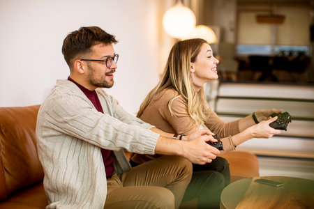 Handsome young couple playing video games at home, sitting on sofa and enjoying themselves