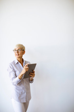 Mature businesswoman using a handheld digital tablet and standing by the wallの写真素材