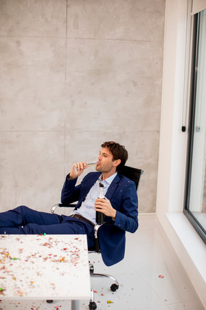 Young business man drinking champagne in the office after Christmas party