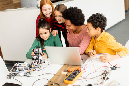 Group of happy kids with their African American female science teacher with laptop programming...