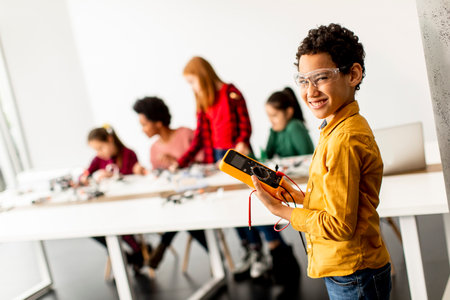 Cute little boy standing in front of  group of kids programming electric toys and robots at robotics...