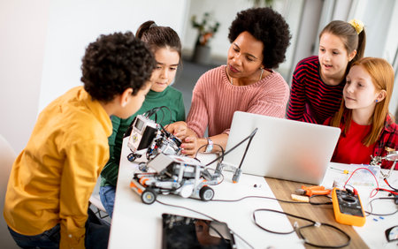 Group of happy kids with their African American female science teacher with laptop programming electric toys and robots at robotics classroomの写真素材