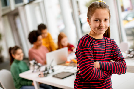 Cute little girl standing in front of  group of kids programming electric toys and robots at robotics classroomの写真素材