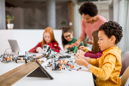 Group of happy kids with their African American female science teacher with laptop programming electric toys and robots at robotics classroomの写真素材