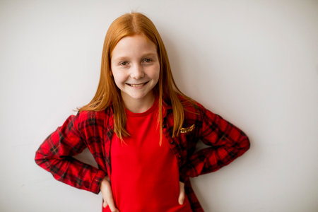 Cute little red hair girl standing by the white wallの写真素材
