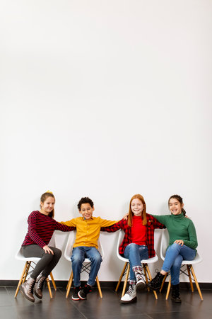 Portrait of cute little kids in jeans  sitting in chairs against the white wallの写真素材