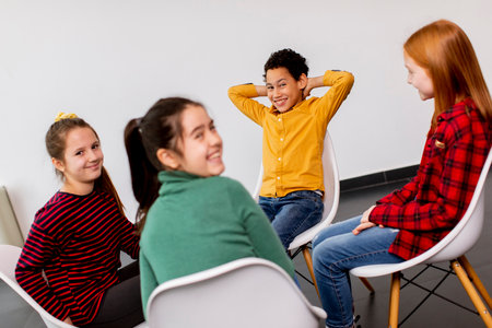 Portrait of cute little kids in jeans talking and sitting in chairs against the white wallの写真素材