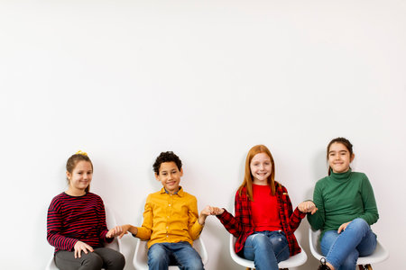 Portrait of cute little kids in jeans  sitting in chairs against the white wall