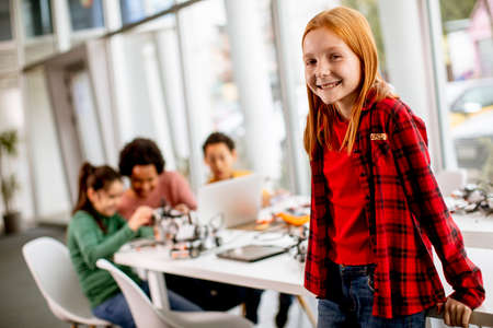 Cute little girl standing in front of  group of kids programming electric toys and robots at robotics classroomの写真素材