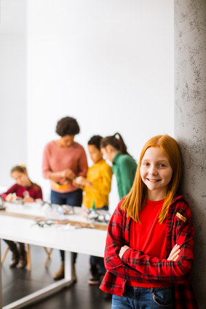 Cute little girl standing in front of  group of kids programming electric toys and robots at...