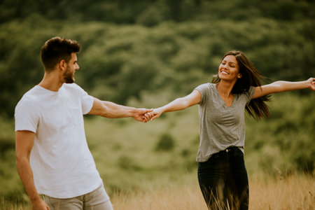 Happy young couple in love walking through grass field on a summer dayの写真素材