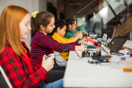 Group of happy kids programming electric toys and robots at robotics classroom