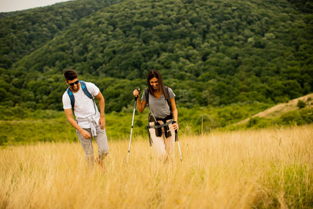 Smiling young couple walking with backpacks over green hills