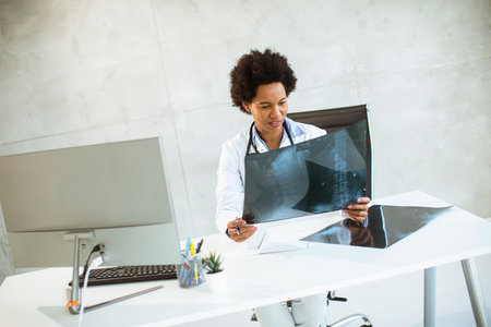 Female African American doctor wearing white coat with stethoscope sitting behind desk in the office...