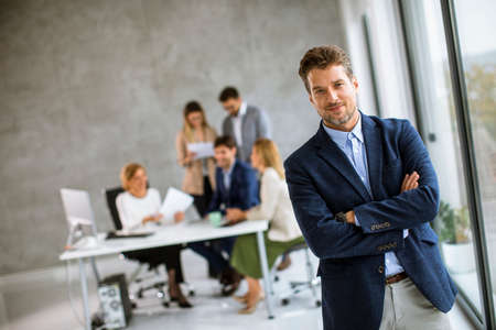 Handsome young business man standing confident in the office in front of his teamの写真素材