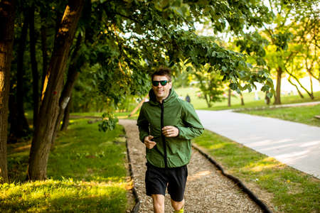 Handsome athletic young man running while doing workout in sunny green parkの写真素材