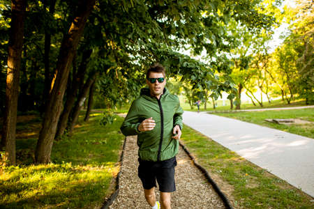 Handsome athletic young man running while doing workout in sunny green parkの写真素材