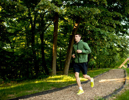 Handsome athletic young man running while doing workout in sunny green park