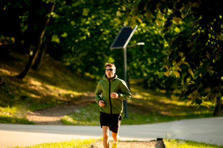 Handsome athletic young man running while doing workout in sunny green park
