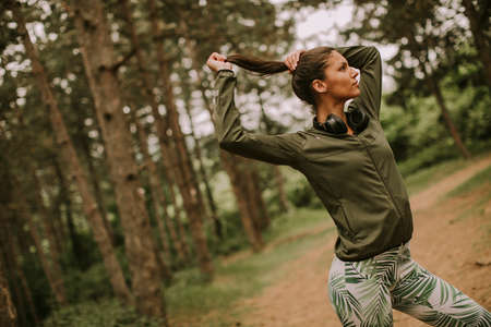Pretty young attractive female runner listening to music and taking a break after jogging in a forestの写真素材