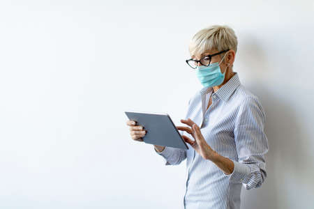 Mature businesswoman using a handheld digital tablet and wear mask to prevent infection by corona virusの写真素材