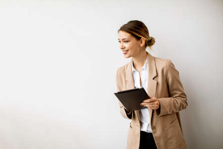 Pretty young woman holding digital tablet by the white wall in modern officeの写真素材