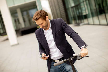 Handsome young businessman using mobile phone on electric scooter