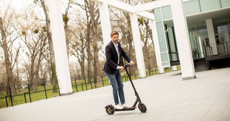 Handsome young business man in a casual clothes riding an electric scooter by an office building on a business meetingの写真素材