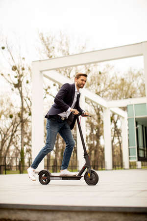 Handsome young business man in a casual clothes riding an electric scooter by an office building on a business meetingの写真素材