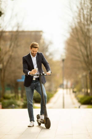 Handsome young businessman using mobile phone  on electric scooterの写真素材