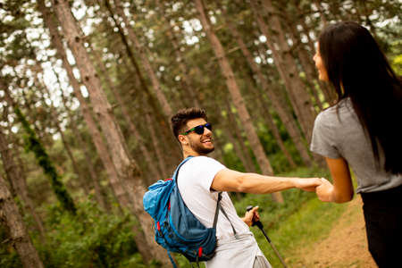 Smiling young couple walking with backpacks in the forest on a summer day