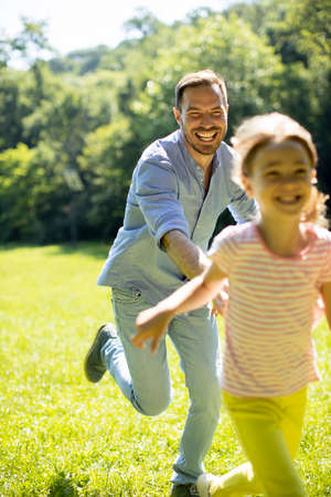 Father chasing his cute little daughter while playing in the parkの写真素材