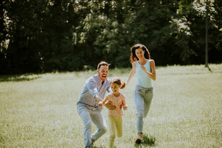 Happy young family with cute little daughter running in park on a sunny dayの写真素材