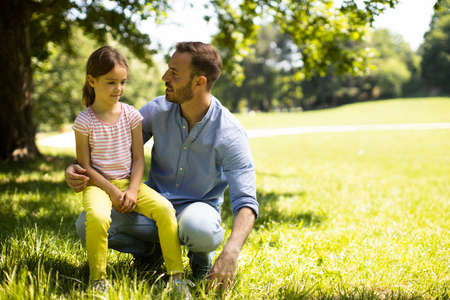 Father with cute little daughter having fun on the grass at the parkの写真素材