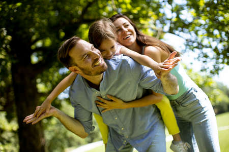 Happy young family with cute little daughter having fun in park on a sunny day